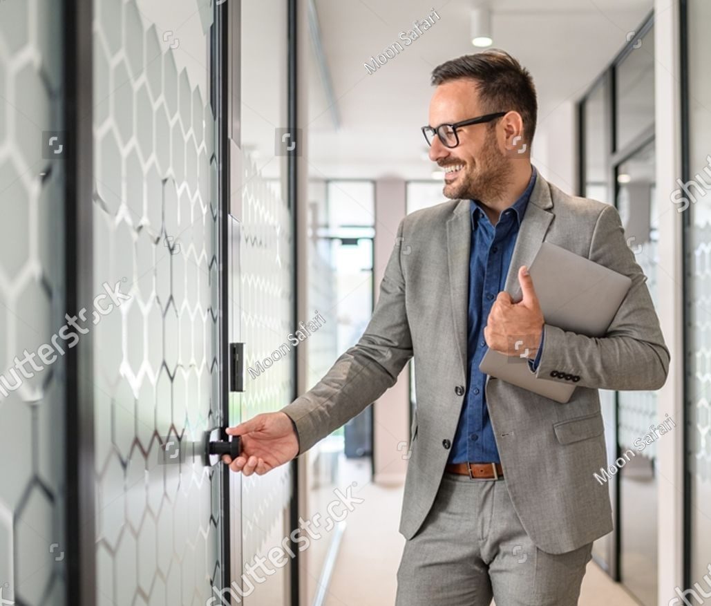 Smiling entrepreneur holding a laptop and opening a glass boardroom door